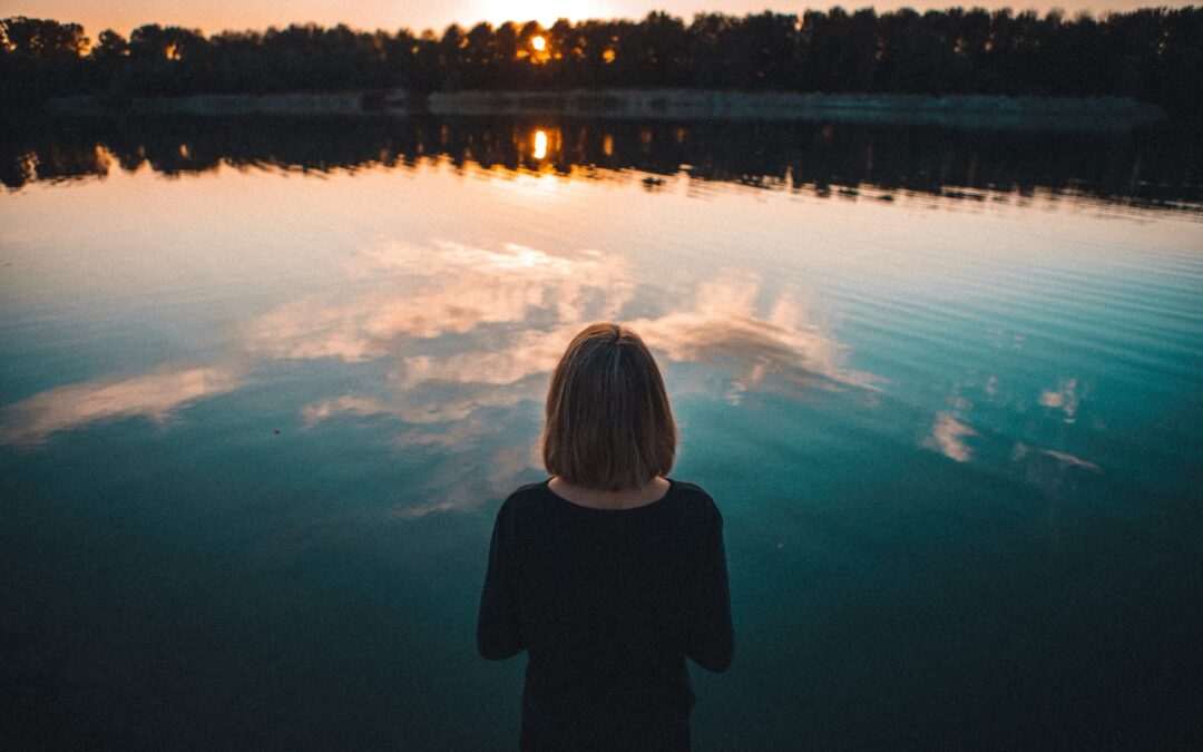 woman looking at calm lake at sunset